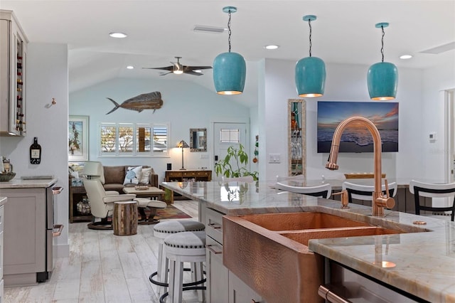 kitchen featuring lofted ceiling, ceiling fan, light stone countertops, light wood-type flooring, and decorative light fixtures