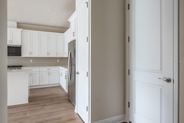 kitchen with white cabinetry, ornamental molding, light wood-type flooring, stainless steel refrigerator, and backsplash