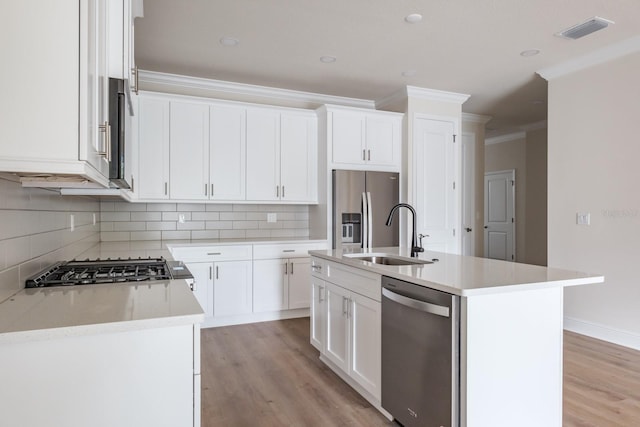 kitchen with stainless steel appliances, sink, white cabinets, ornamental molding, and a kitchen island with sink