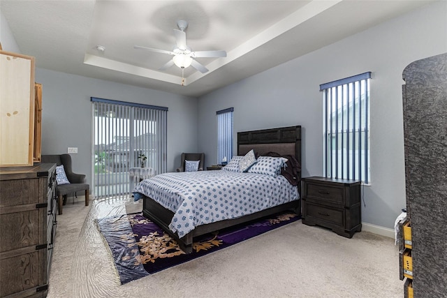 bedroom with multiple windows, light colored carpet, ceiling fan, and a raised ceiling