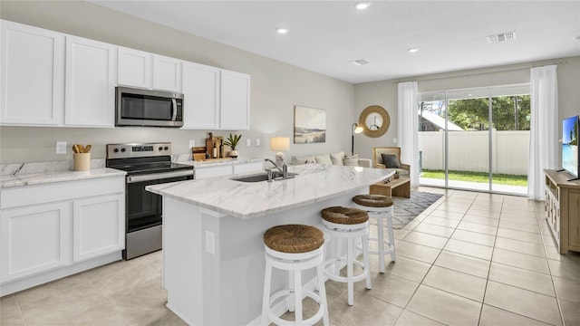 kitchen with stainless steel appliances, light stone countertops, white cabinets, and a center island with sink