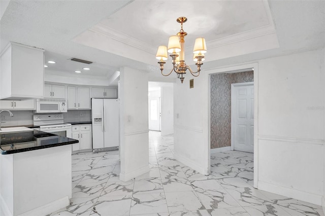 kitchen featuring white cabinetry, decorative light fixtures, a tray ceiling, white appliances, and a chandelier