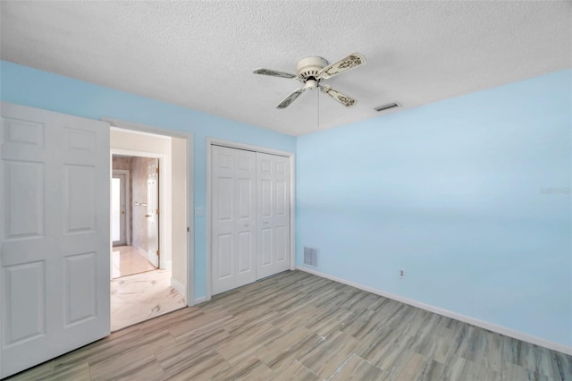 unfurnished bedroom with ceiling fan, a textured ceiling, a closet, and light wood-type flooring