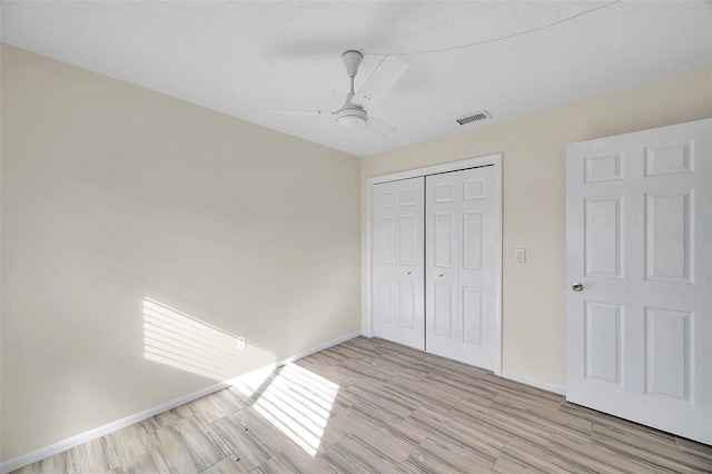 unfurnished bedroom featuring ceiling fan, a textured ceiling, a closet, and light wood-type flooring