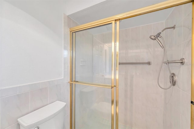 bathroom featuring toilet, tile walls, and a shower with door