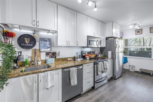 kitchen with stainless steel appliances, white cabinetry, sink, dark stone countertops, and light wood-type flooring