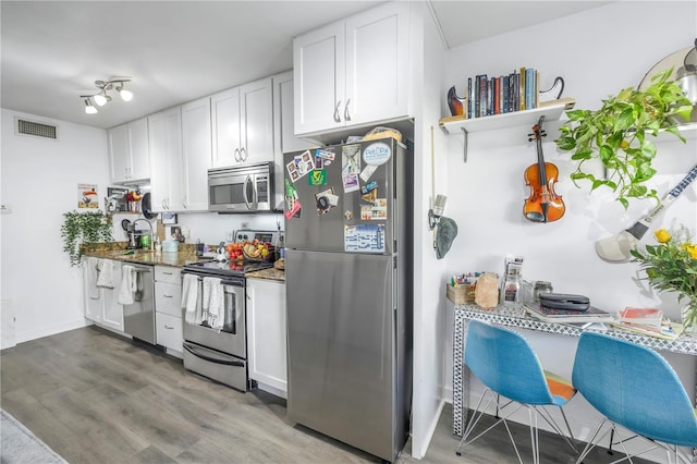 kitchen with dark stone countertops, appliances with stainless steel finishes, hardwood / wood-style floors, and white cabinets