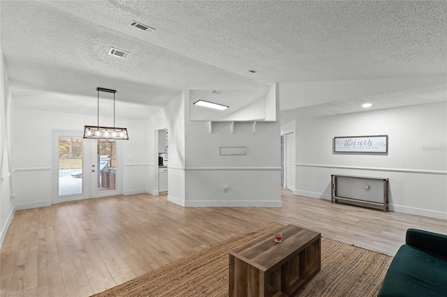 unfurnished living room with a textured ceiling, french doors, vaulted ceiling, and light wood-type flooring