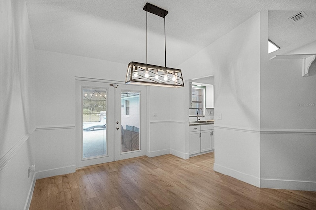 unfurnished dining area featuring lofted ceiling, french doors, sink, light hardwood / wood-style flooring, and a textured ceiling