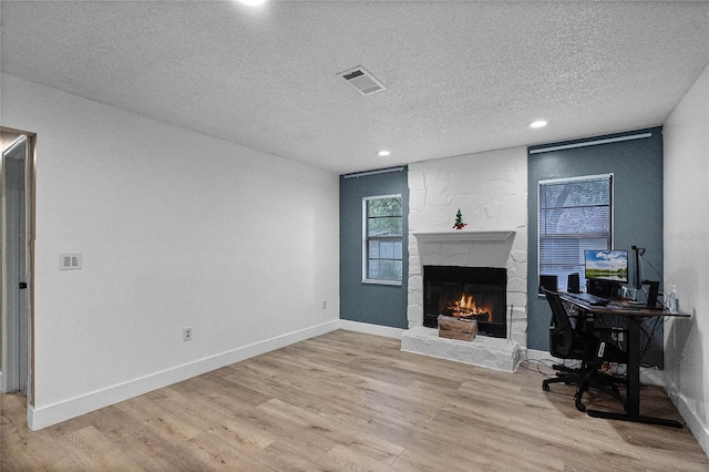 home office with a fireplace, a textured ceiling, and light hardwood / wood-style floors