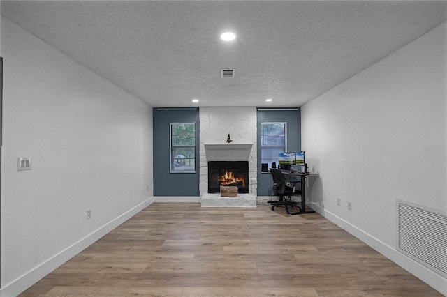 unfurnished office featuring a stone fireplace, a textured ceiling, and light hardwood / wood-style flooring