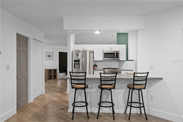 kitchen featuring white cabinetry, stainless steel appliances, light hardwood / wood-style flooring, kitchen peninsula, and a breakfast bar area