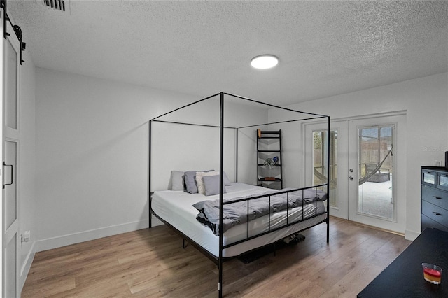 bedroom featuring access to outside, a barn door, a textured ceiling, and light wood-type flooring