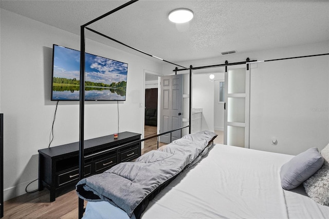 bedroom with hardwood / wood-style floors, ensuite bathroom, a barn door, and a textured ceiling