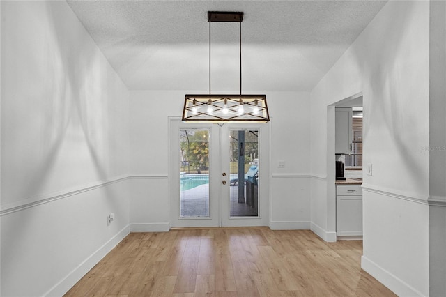 unfurnished dining area with light hardwood / wood-style floors, lofted ceiling, a textured ceiling, and french doors