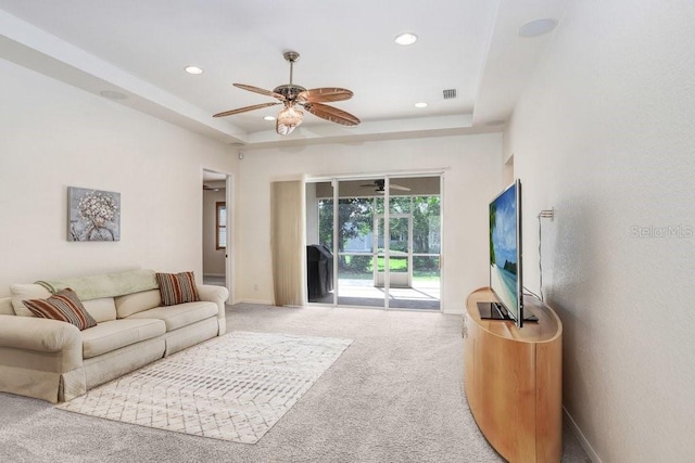 living room with a tray ceiling, carpet flooring, visible vents, and baseboards