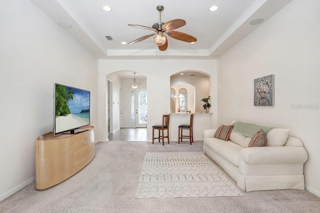 living room with ceiling fan, light carpet, and a raised ceiling