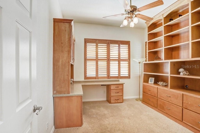 home office with built in desk, ceiling fan, and light carpet