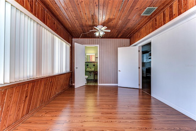 empty room featuring hardwood / wood-style floors, wood walls, ceiling fan, and wooden ceiling