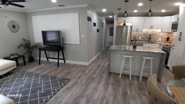 kitchen featuring appliances with stainless steel finishes, hanging light fixtures, light stone countertops, a breakfast bar, and white cabinets