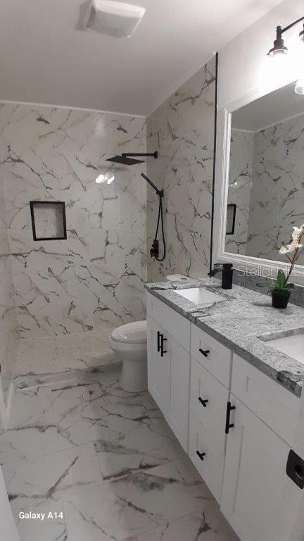 bathroom featuring toilet, tiled shower, and vanity