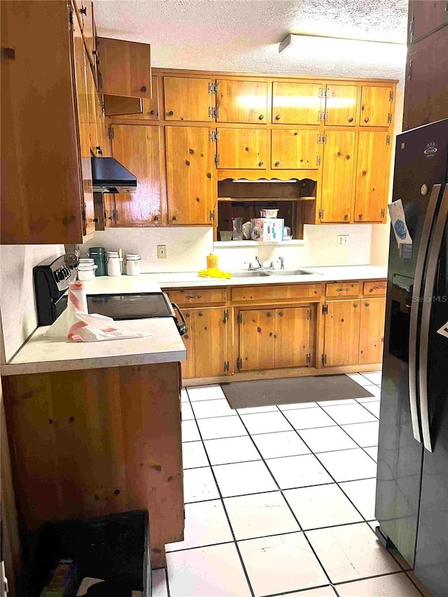 kitchen with stove, a textured ceiling, black fridge, and sink