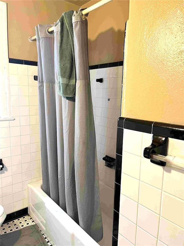 bathroom with tile walls, toilet, shower / bath combo with shower curtain, and tile patterned floors