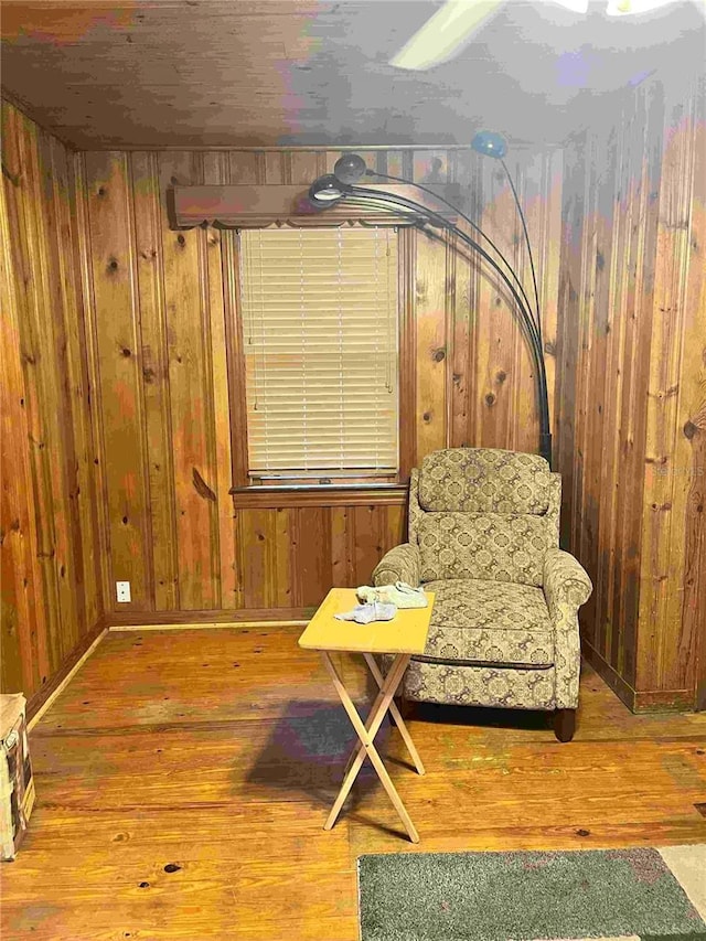 sitting room with hardwood / wood-style flooring and wooden walls