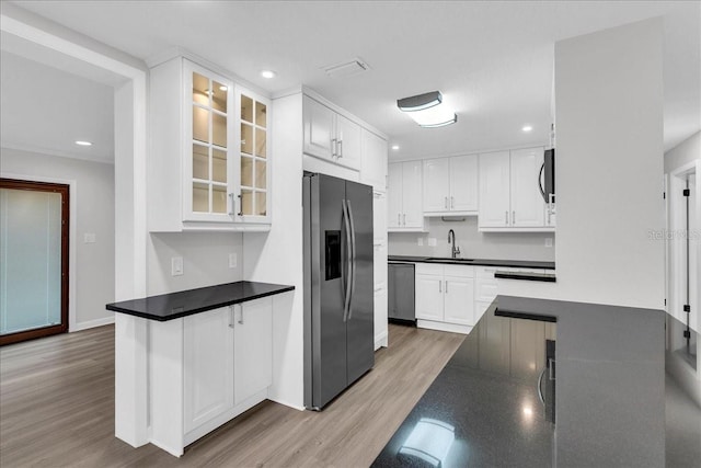 kitchen with sink, kitchen peninsula, appliances with stainless steel finishes, white cabinets, and light wood-type flooring