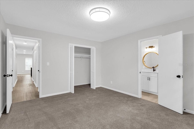 unfurnished bedroom with connected bathroom, a closet, a textured ceiling, and light colored carpet