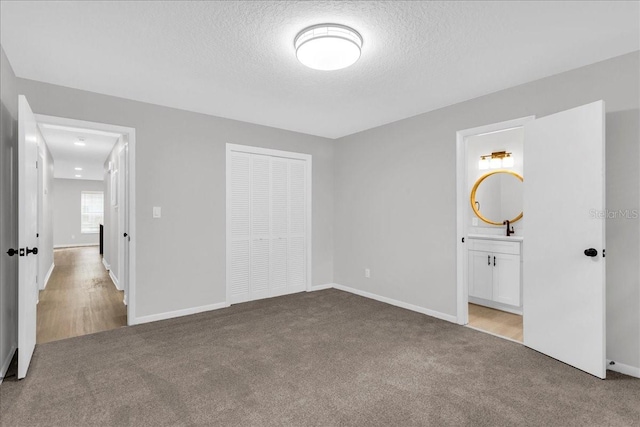 unfurnished bedroom with a closet, a textured ceiling, light carpet, and ensuite bathroom