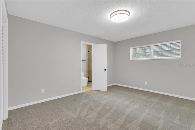 unfurnished bedroom featuring connected bathroom, a textured ceiling, and light carpet