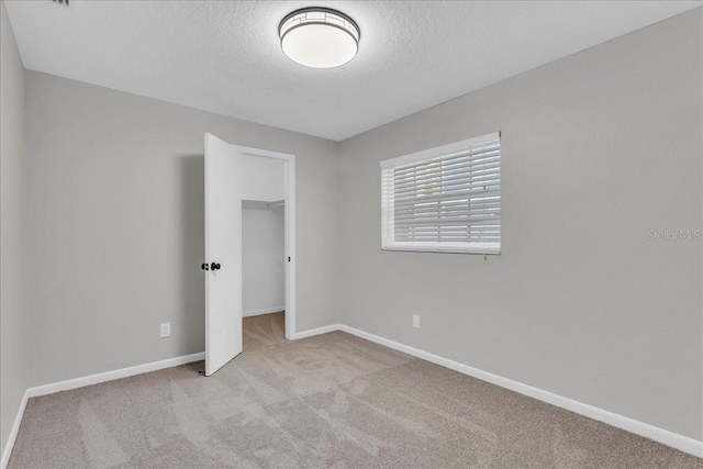 unfurnished bedroom featuring light colored carpet, a textured ceiling, a walk in closet, and a closet