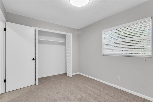 unfurnished bedroom featuring light colored carpet, a textured ceiling, and a closet