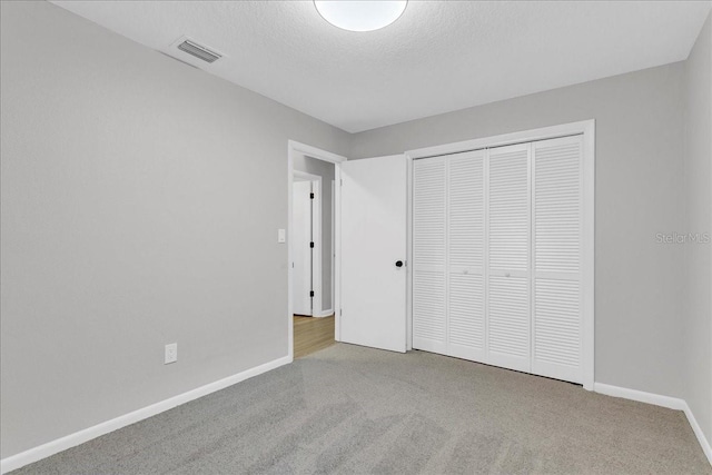 unfurnished bedroom with light colored carpet, a textured ceiling, and a closet