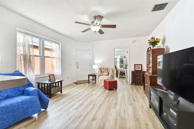 living room featuring light wood-type flooring, a textured ceiling, and ceiling fan