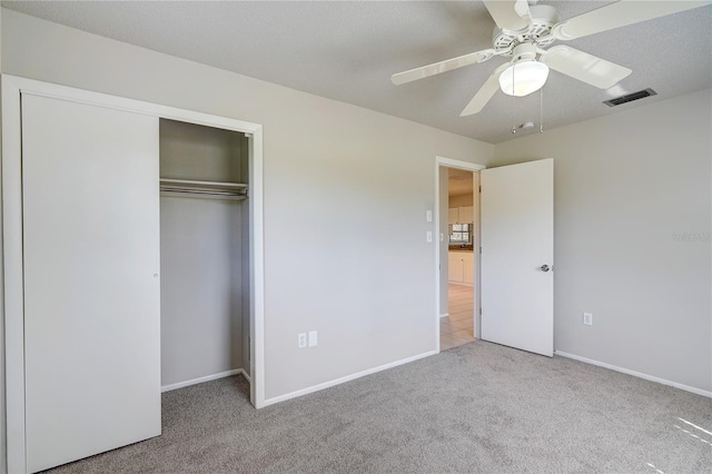 unfurnished bedroom with a closet, ceiling fan, light carpet, and a textured ceiling