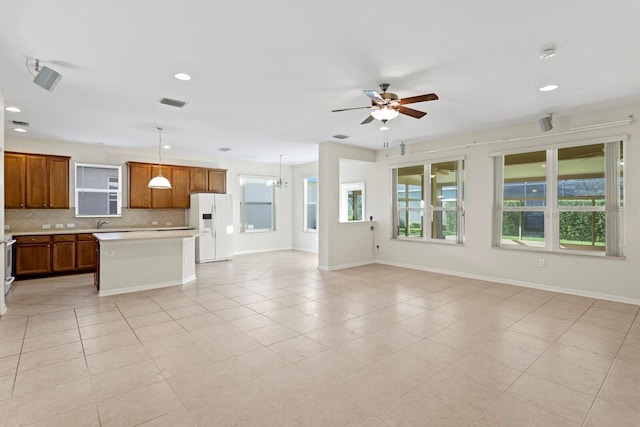 kitchen featuring ceiling fan with notable chandelier, white refrigerator with ice dispenser, light tile patterned floors, decorative light fixtures, and a kitchen island