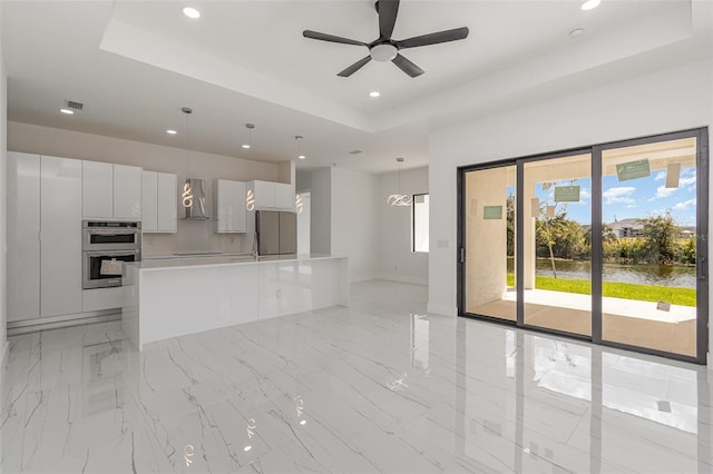 unfurnished living room featuring ceiling fan and a tray ceiling