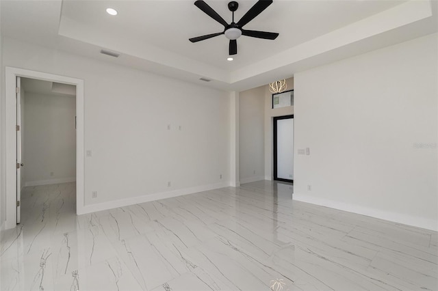 empty room with ceiling fan and a raised ceiling