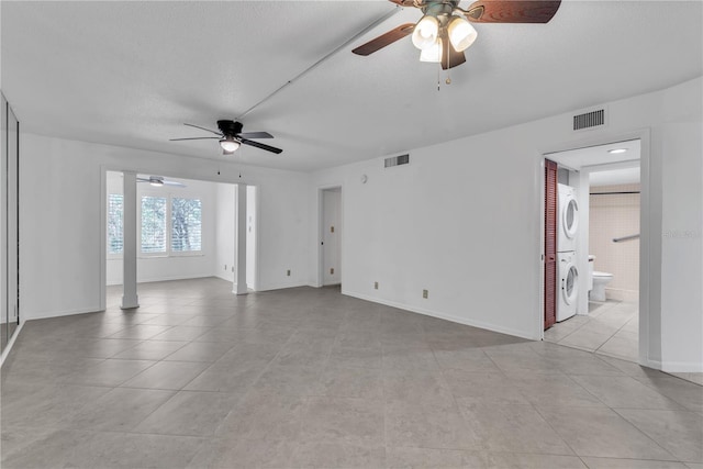 empty room with a textured ceiling, ceiling fan, light tile patterned flooring, and stacked washer / dryer