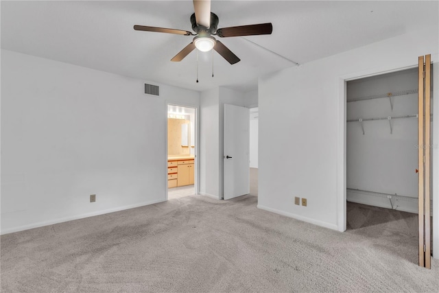 unfurnished bedroom featuring ceiling fan, a closet, light colored carpet, and ensuite bath