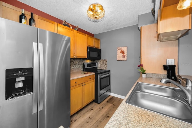 kitchen featuring sink, tasteful backsplash, light hardwood / wood-style floors, a textured ceiling, and appliances with stainless steel finishes