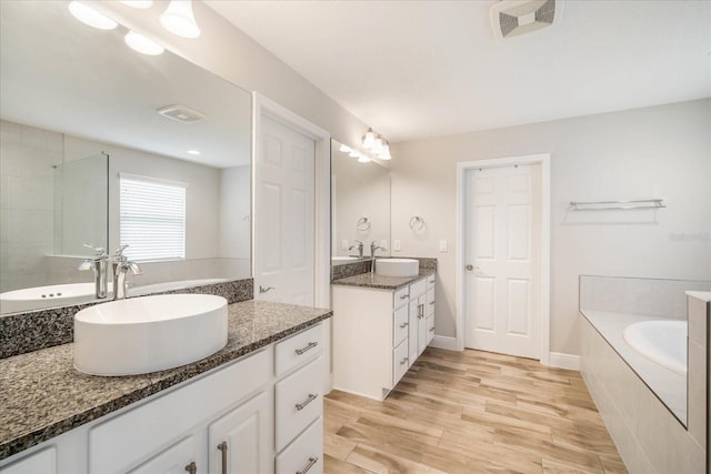 bathroom featuring wood-type flooring, tiled tub, and vanity