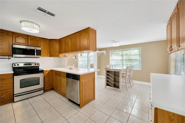 kitchen with kitchen peninsula, a textured ceiling, light tile patterned floors, and appliances with stainless steel finishes