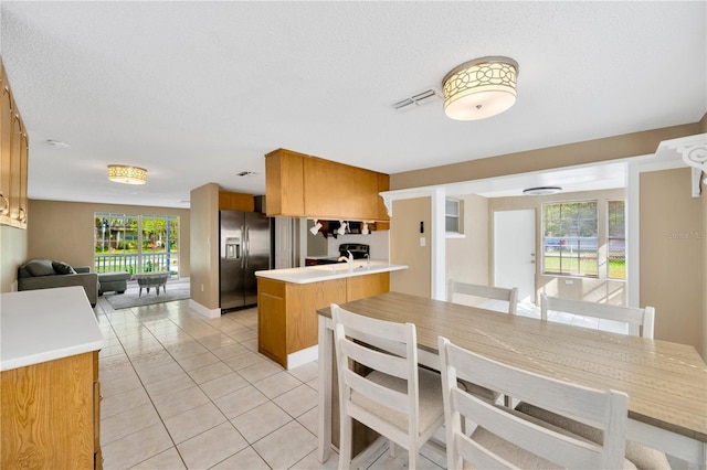 kitchen with stainless steel fridge with ice dispenser, a textured ceiling, light tile patterned floors, and kitchen peninsula