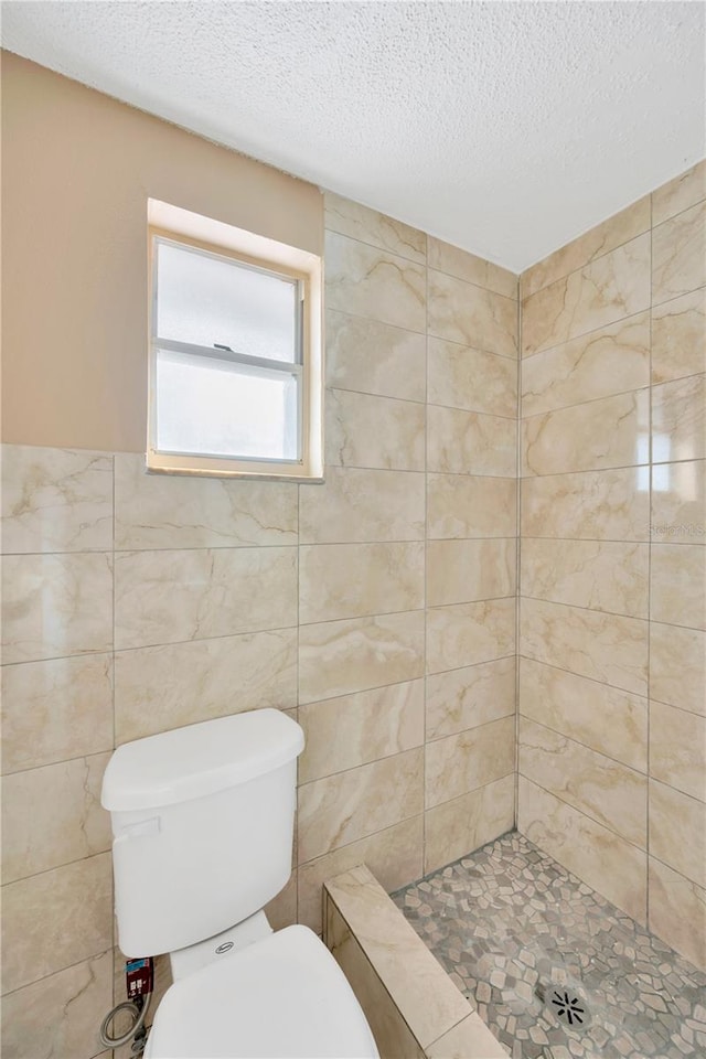 bathroom with tile walls, tiled shower, a textured ceiling, and toilet