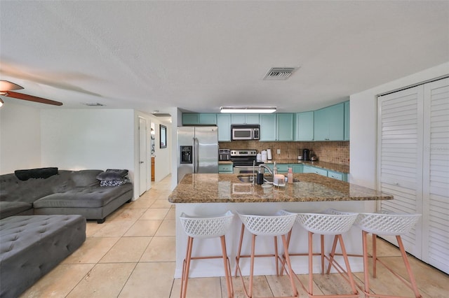 kitchen featuring stainless steel appliances, light tile patterned floors, tasteful backsplash, a kitchen breakfast bar, and stone countertops