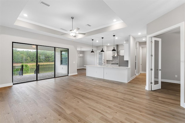 kitchen with pendant lighting, white cabinets, a tray ceiling, wall chimney exhaust hood, and light hardwood / wood-style flooring