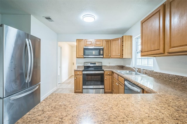 kitchen featuring a textured ceiling, sink, light wood-type flooring, and appliances with stainless steel finishes